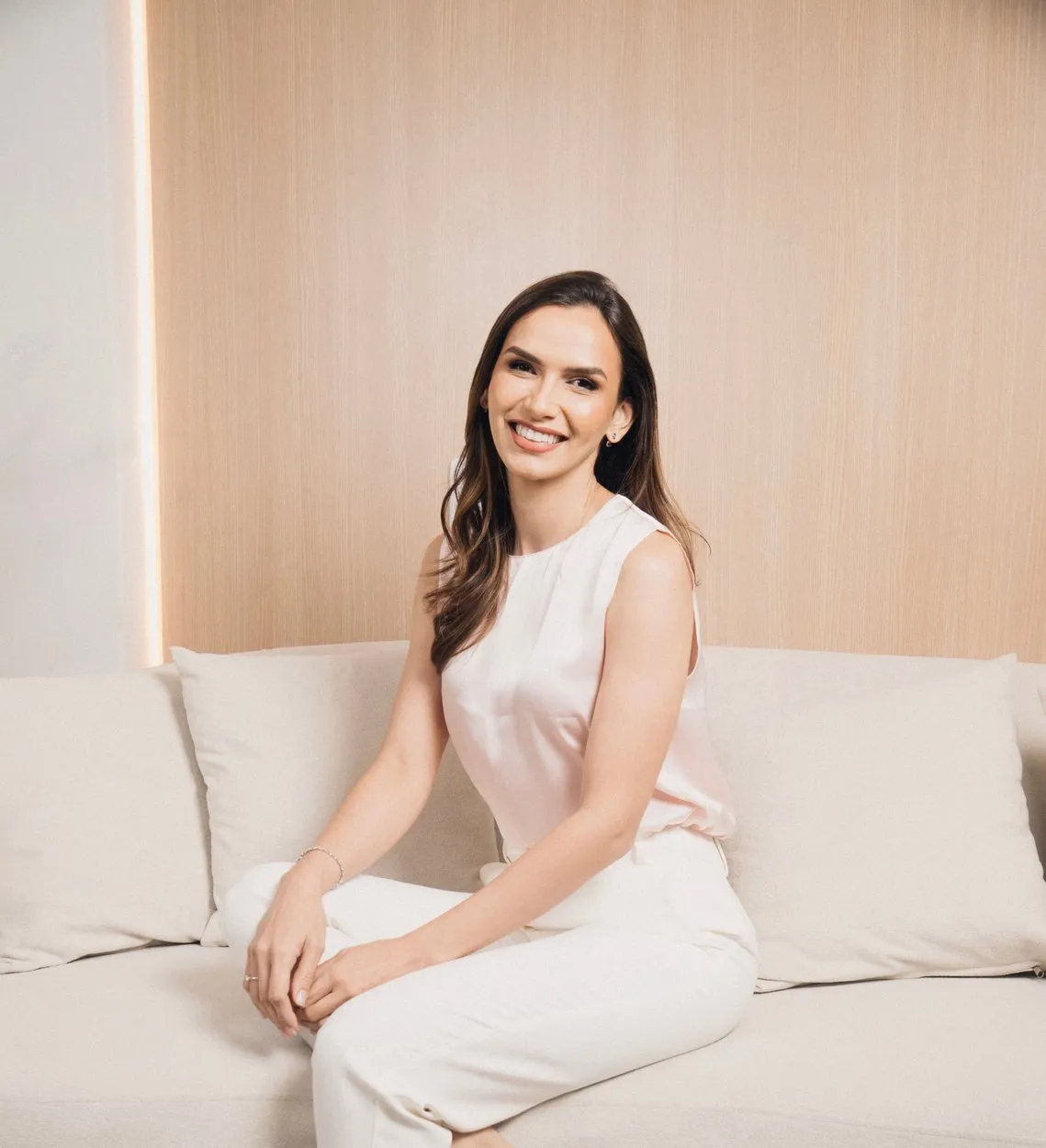 Dra. Anne Caroline Amorim, ginecologista, sentada em um sofá claro